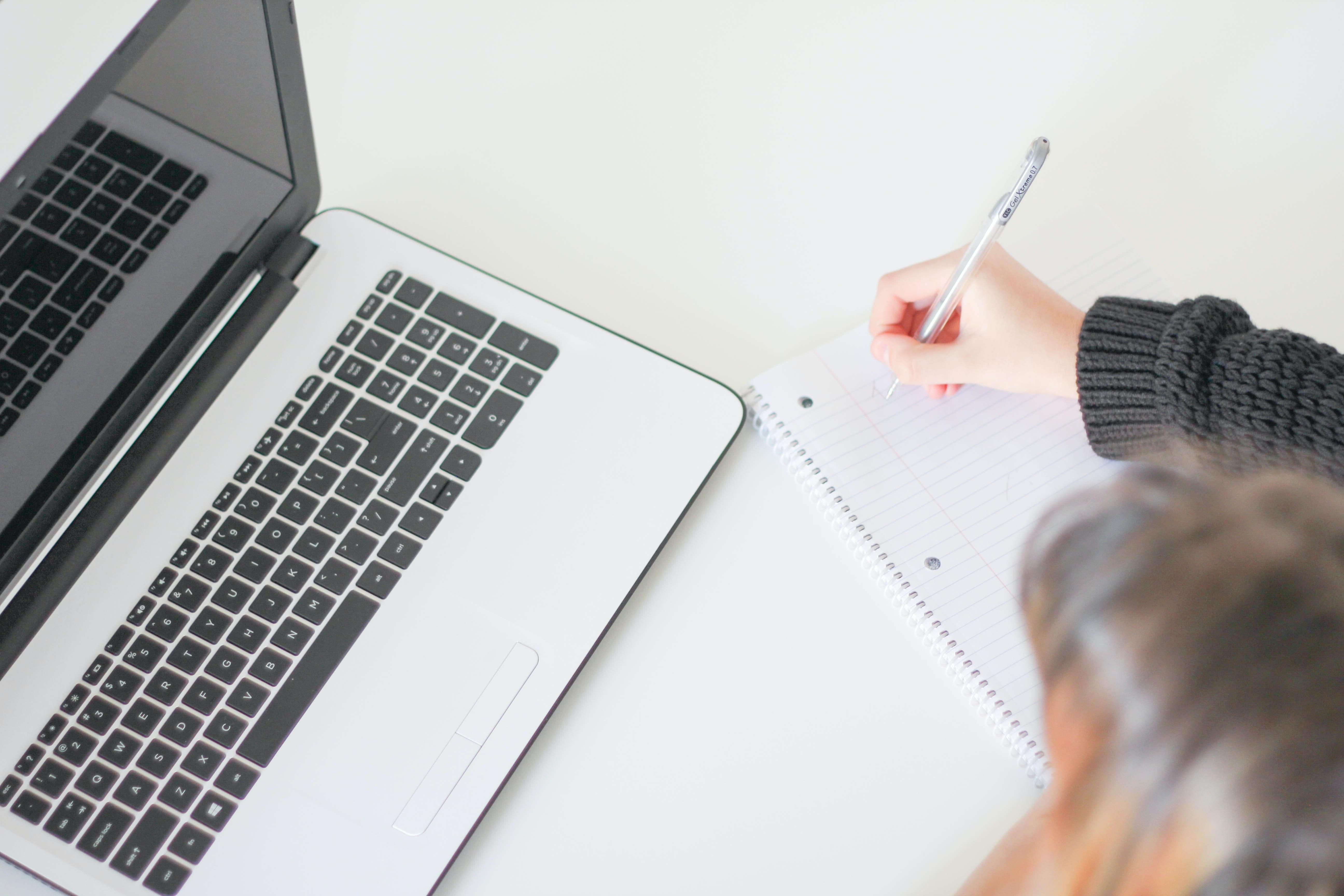 Mujer concentrada anotando en un cuaderno con el portatil delante. Foto de J. Kelly Brito en Unsplash